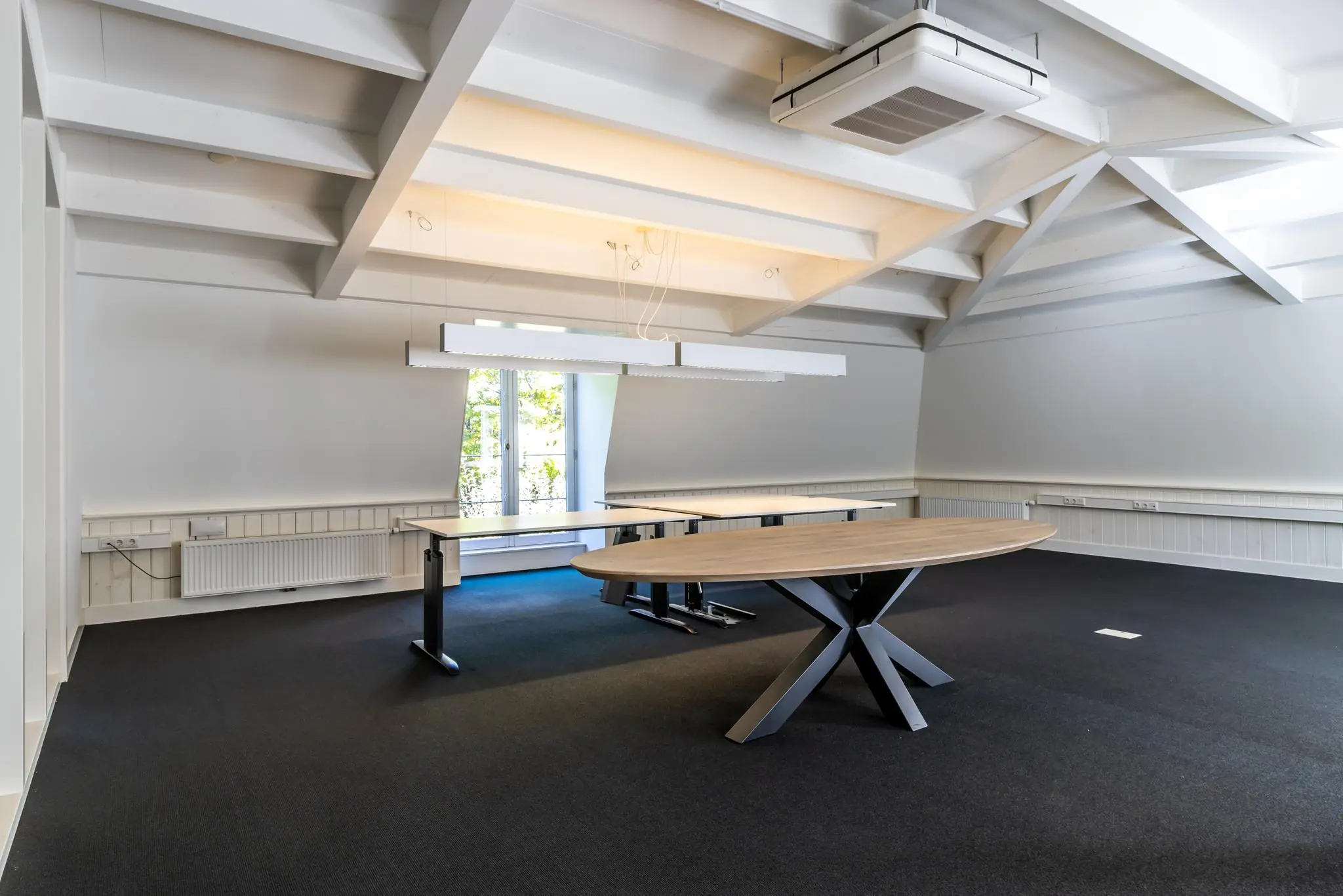 Moderne vergaderruimte aan de Langbroekerdijk met houten tafels, zwarte vloerbedekking en zichtbare dakconstructie.